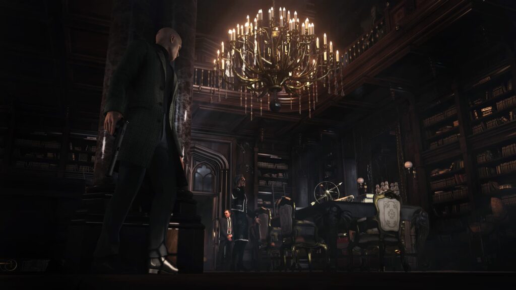 Agent 47 hides behind a wall in a large room with a chandelier hanging from the ceiling.
