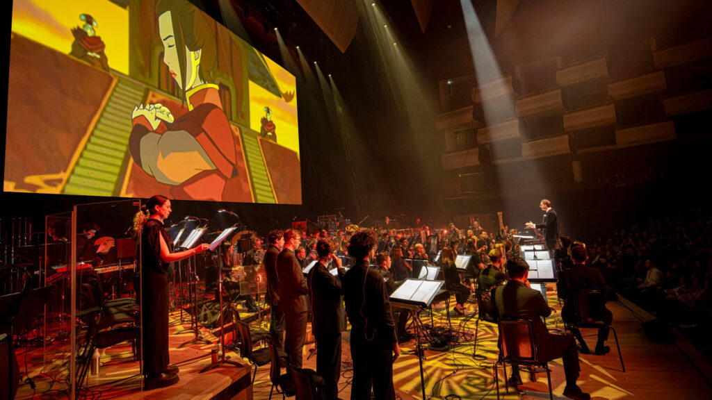 Taken by Zdenko Hanout during the Avatar: The Last Airbender In Concert World Premiere. Depicts the full orchestra playing while a clip of Azula training is projected onto a large screen behind them.