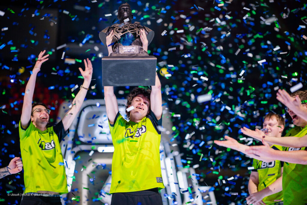 The photo features the Rainbow Six Siege X team M80 lifting the trophy at the esports tournament R6 Munich Major 2025.